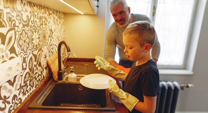 Un niño lava los platos para ayudar en las tareas domésticas