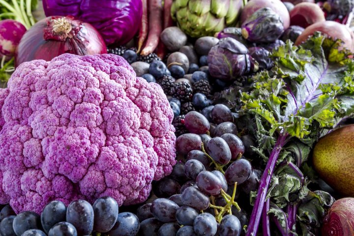 Composición de frutas y verduras azules y moradas, incluyendo uvas, ciruelas, bayas, cebollas rojas y col morada.